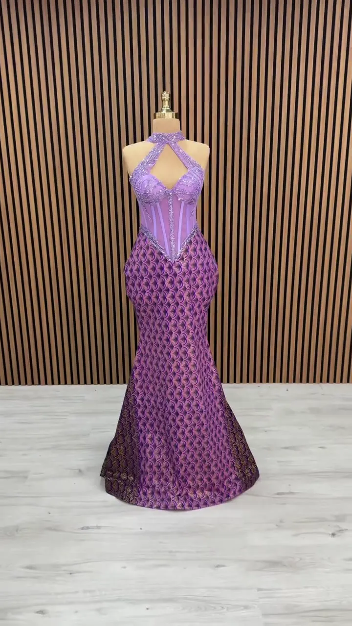 Çapraz halter dalga desenli balık abiye, ahşap çıtalı duvar önünde önden; mor etek ve lila korsaj.