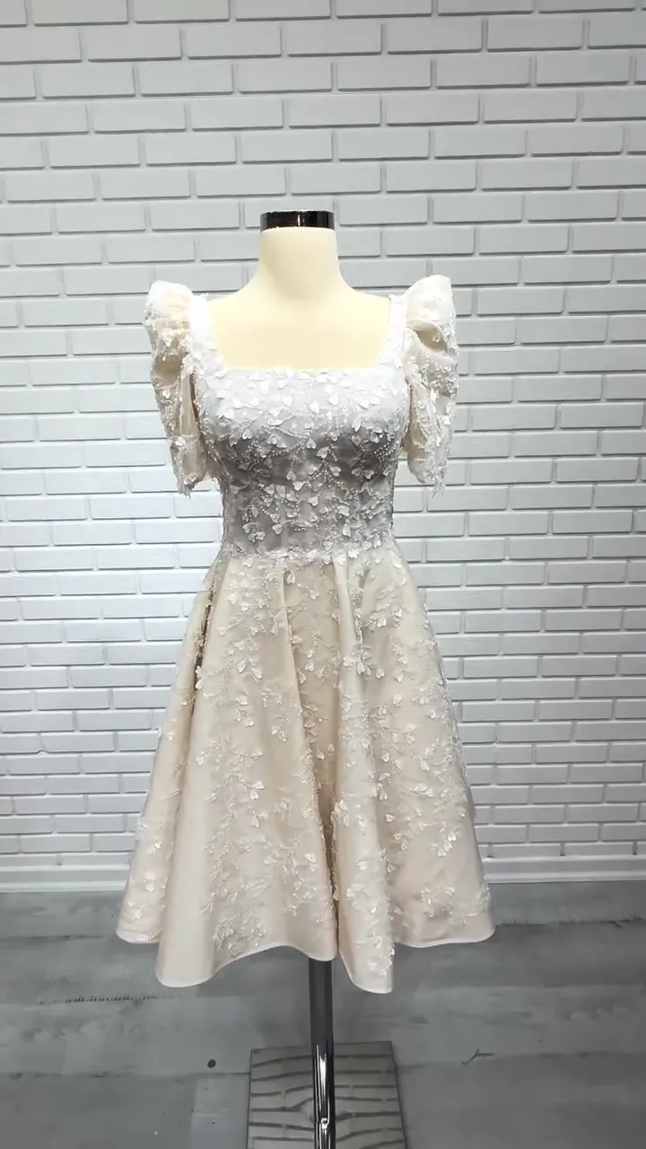 Kare yaka kabarık kollu mini after party elbisesi, kırık beyaz ve krem tonlarında tuğla duvar önünde önden.