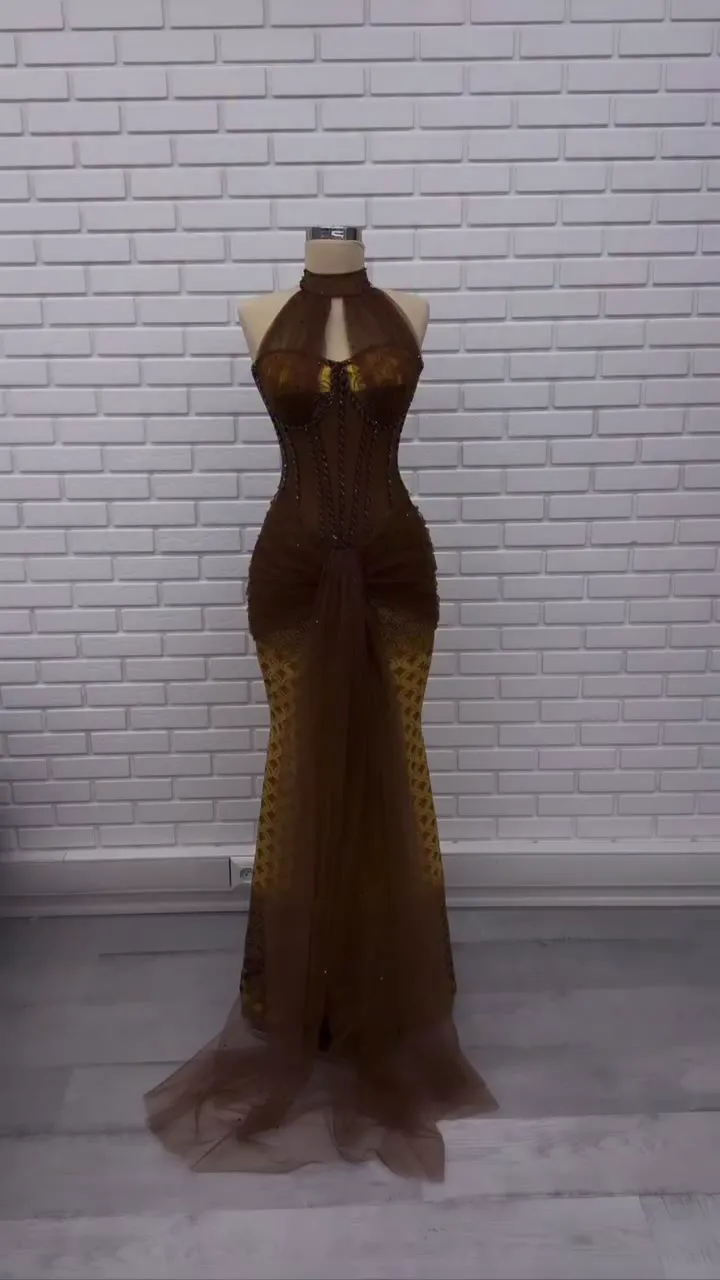 Damla halter desenli dar etek abiye önden; beyaz tuğla duvar önünde kahverengi gövde ve altın tonlu etek.