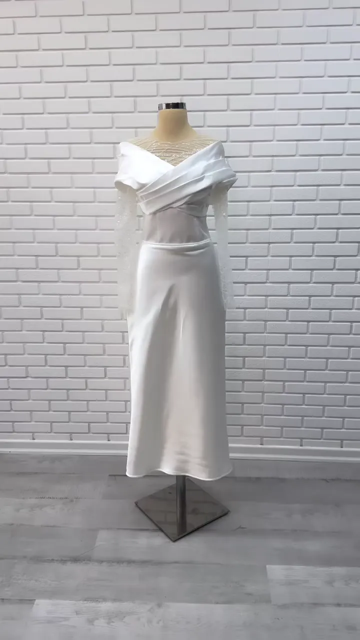 Çapraz drapeli illüzyon yaka midi nikah elbisesi, beyaz renkte tuğla duvar önünde önden; uzun saydam kollar.