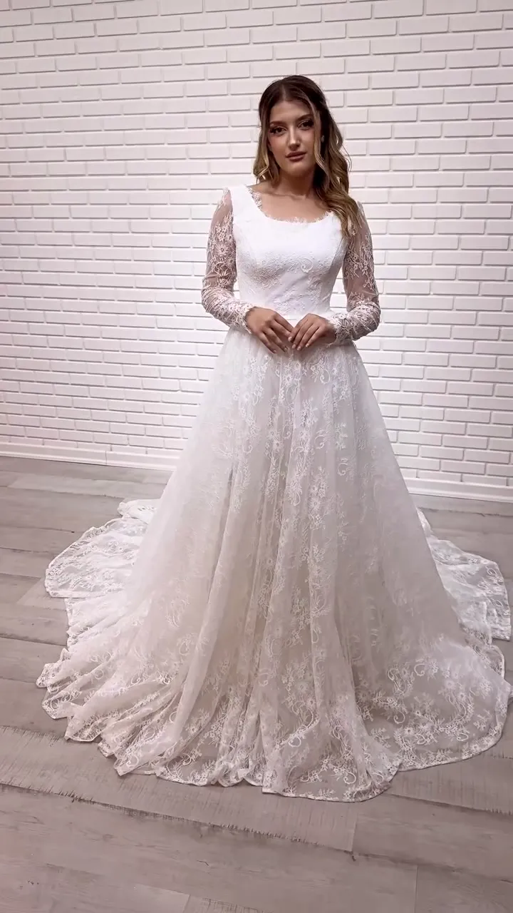Kare yaka opak korsaj dantel A kesim gelinlik, tuğla duvar önünde model üzerinde önden.